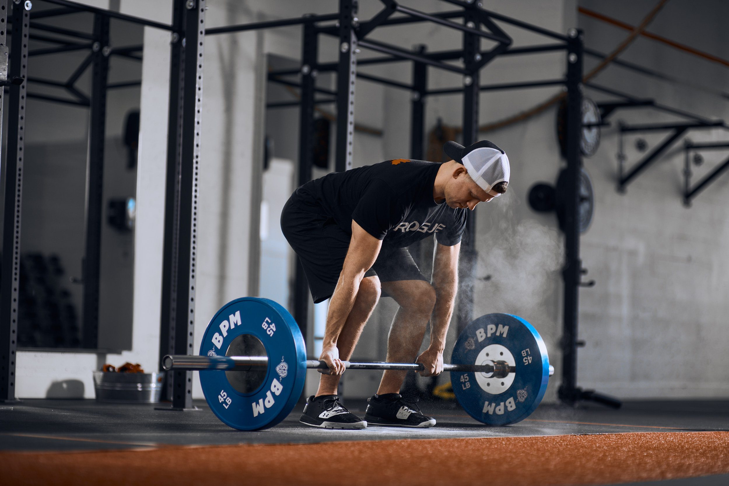 A man prepares to Olympic lift a barbell at BPM, demonstrating focus and proper technique in a gym setting