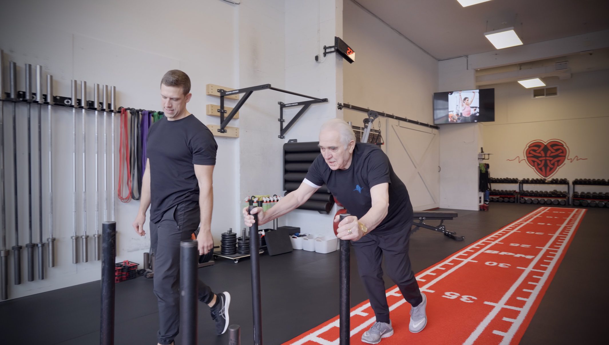 An older male personal training client pushes a sled with a personal trainer in Victoria, BC